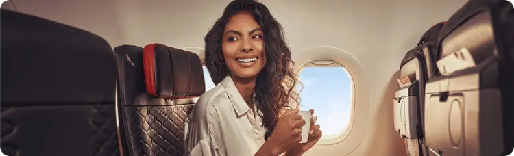 A woman on a plane, smiling and enjoying a cup of coffee